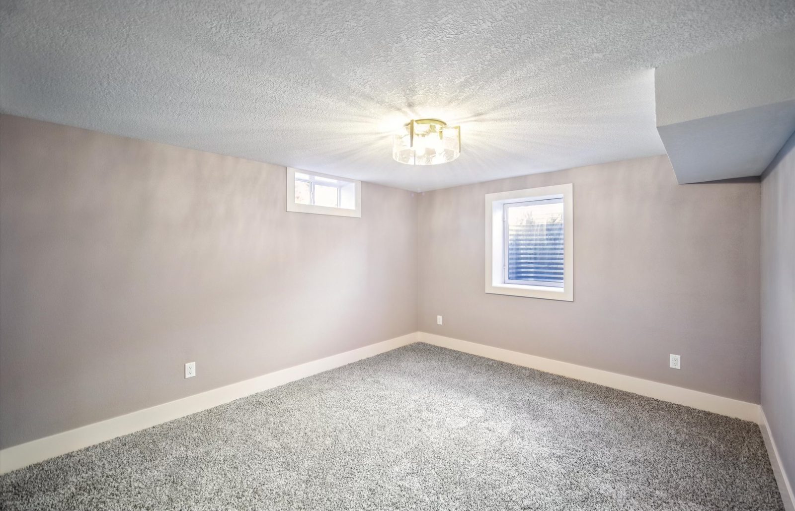 Bright finished basement room with egress window and gold ceiling light