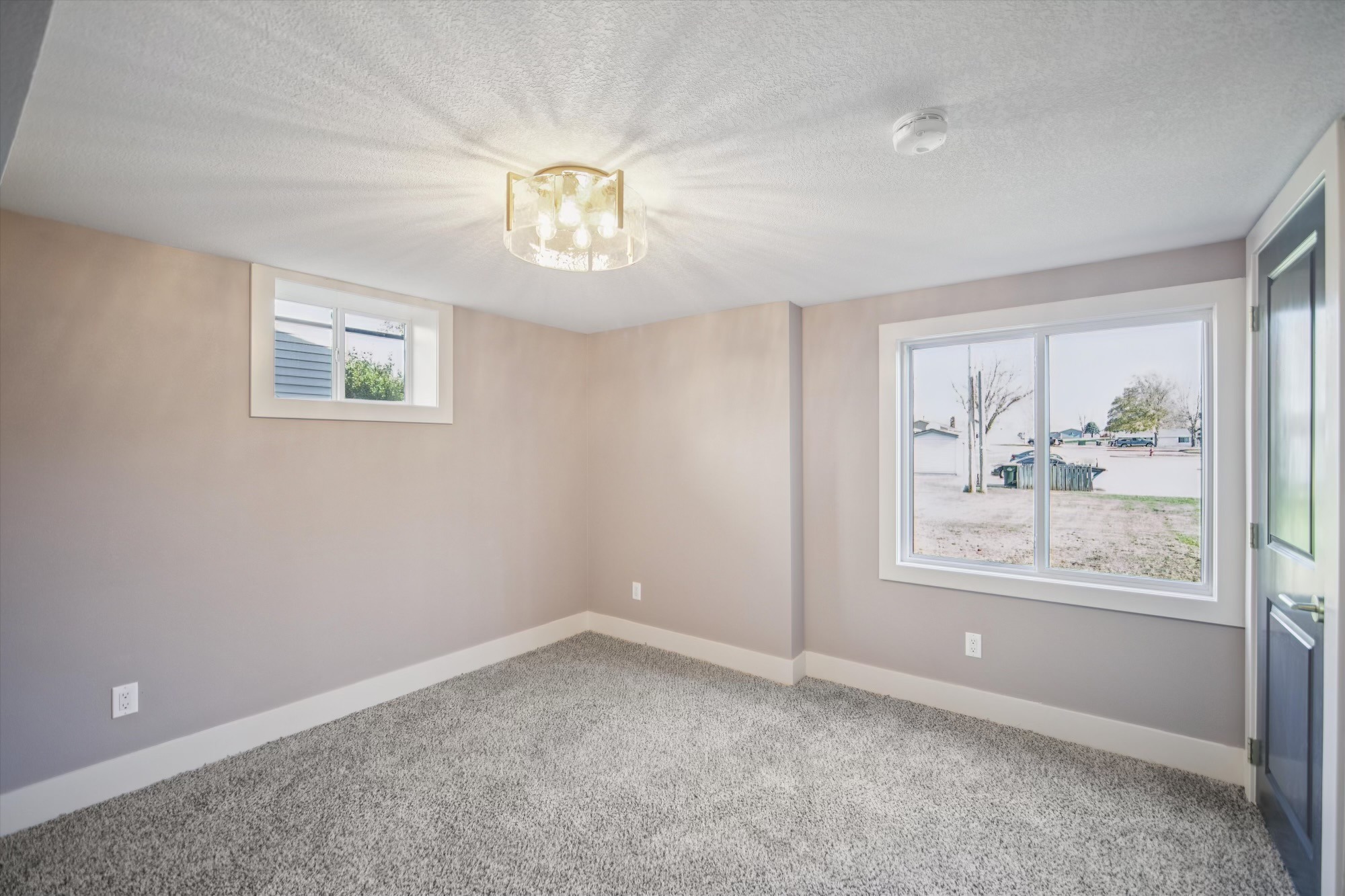 Finished basement room with carpet, white trim, and new lighting